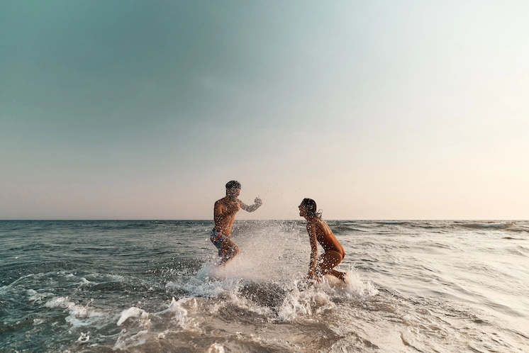 Offers 2 Playful couple splashing in the ocean at sunset, embracing adventure and relaxation on the Outer Banks.