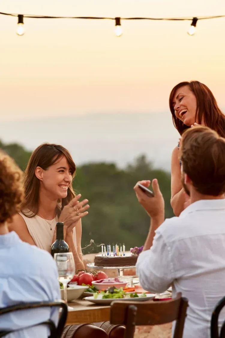 Meetings 2 Friends celebrating a birthday with food and drinks at sunset at The Sanderling Hotel – joyful outdoor gathering.